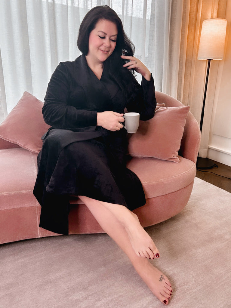 MsLindsayM, a plus size woman sitting on a pink chaise lounger drinking a cup of tea wearing a black velvet plus size robe.