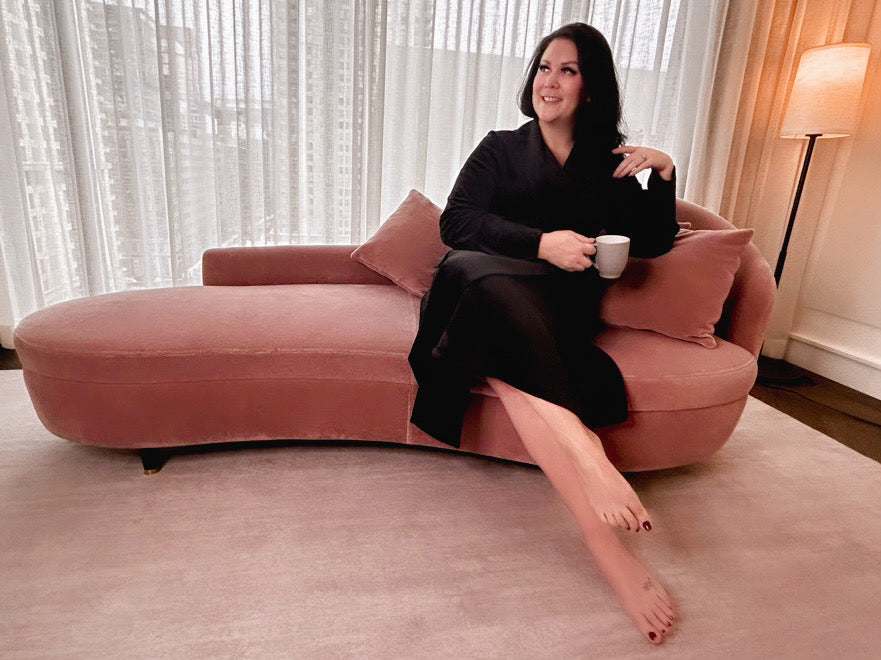 MsLindsayM, a plus size woman sitting on a pink chaise lounger drinking a cup of tea wearing a black velvet plus size robe.